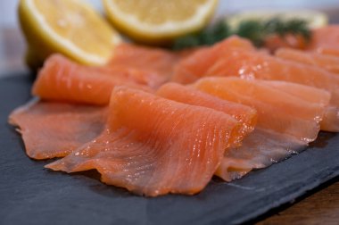 Slices of tasty smoked Scottish salmon fish served on black plate with lemon and fresh dill close up