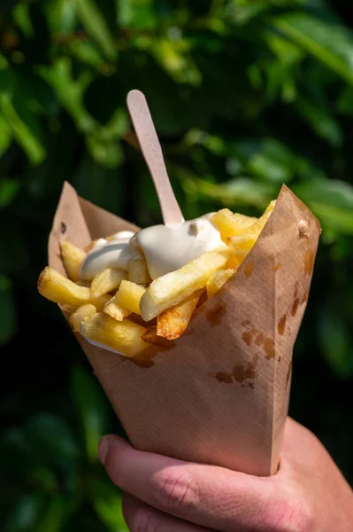 Traditional street food in Belgium and Netherlands, French fried potatoes chips with mayonnaise sauce in paper cone bag