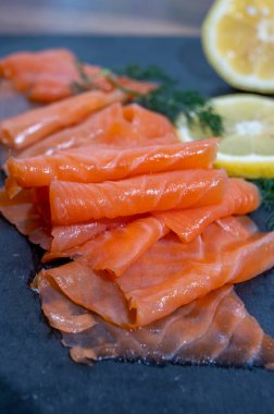 Slices of tasty smoked Scottish salmon fish served on black plate with lemon and fresh dill close up