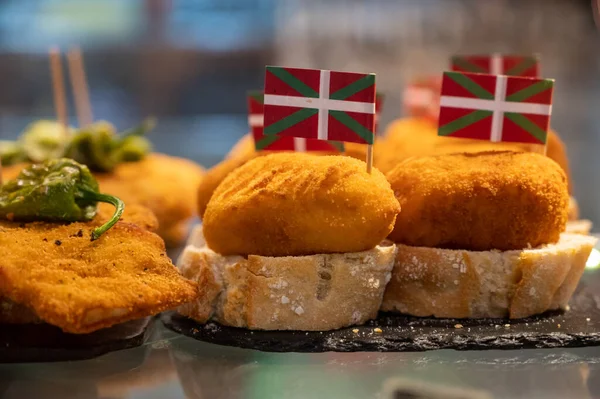 Typical snack in bars of Basque Country, pinchos or pinxtos, small fried croquette with squid and flag of Basque Country, San Sebastian, Spain, close up