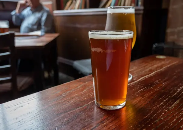 Pint glasses of cold fresh british ale and lager beer served in old vintage English pub