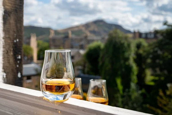 Glass of single malt scotch whisky served on old white window sill in Scottisch house with view on old part of Edinburgh and hills, Scotland, UK, dram of speyside whisky