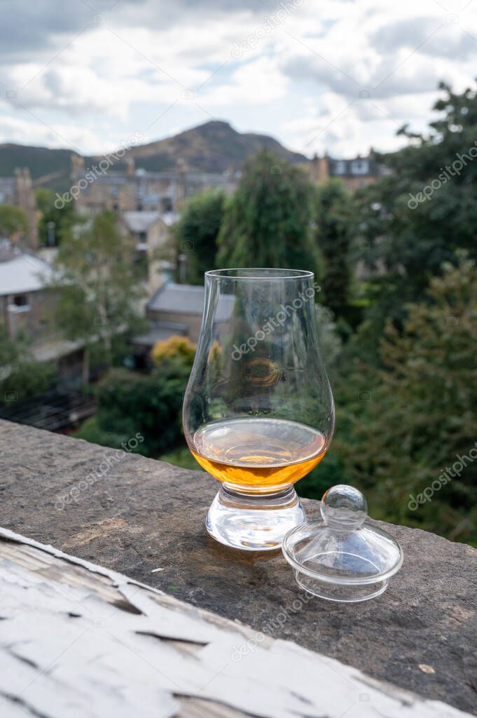 Glass of single malt scotch whisky served on old window sill in Scottisch house with view on old part of Edinburgh city, Scotland, UK, dram of blended whiskey
