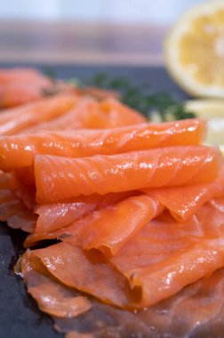 Slices of tasty smoked Scottish salmon fish served on black plate with lemon and fresh dill close up