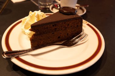 Meşhur Sachertorte çikolatalı pastası. Kayısı reçeli ve beyaz tahtada krem şanti ile servis ediliyor.