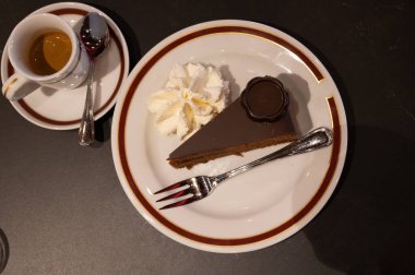 Avusturya kaynaklı kayısı reçelli Sachertorte çikolatalı pastasından bir parça. Sütlü beyaz tahtada krema ve siyah kahve ile servis ediliyor.
