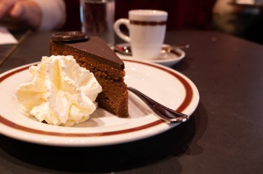 Meşhur Sachertorte çikolatalı pastası. Kayısı reçeli ve beyaz tahtada krem şanti ile servis ediliyor.