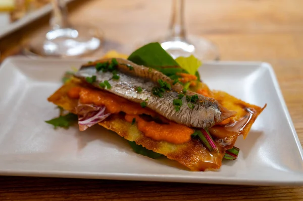 Spanish food, one tapas small piece of roasted bread cracker with vegetables puree and smoked sardine fish, close up