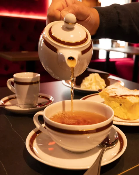Tea time in England, pouring of black earl grey tea with bergamot in cup, high tea served cafe in London, close up