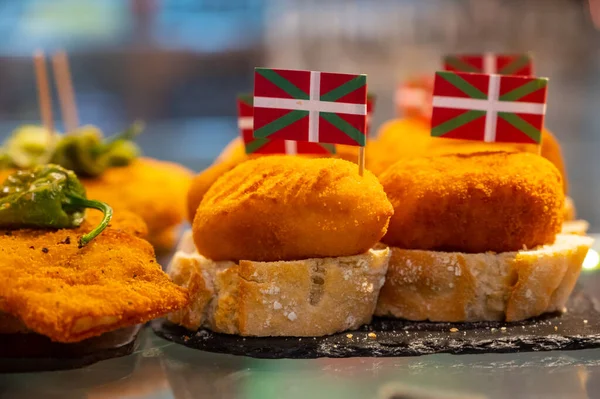 Typical snack in bars of Basque Country, pinchos or pinxtos, small fried croquette with squid and flag of Basque Country, San Sebastian, Spain, close up