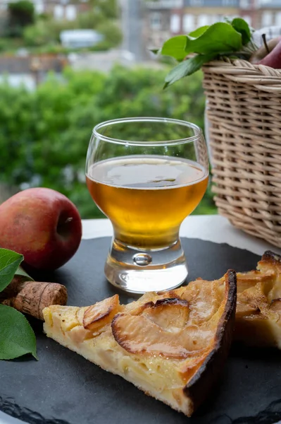 Apple products of Normandy region, homemade baked apple cake, glass of cider drink and houses of Etretat village on background, Normandy, France