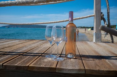Provence 'den getirilen bardaklar ve bir şişe soğuk gül şarabı mavi deniz manzaralı ahşap yat iskelesinde ve Saint-Tropez yakınlarındaki plaj plajı Plage de Pampelonne, Fransa' da yaz tatili