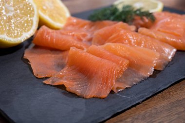 Slices of tasty smoked Scottish salmon fish served on black plate with lemon and fresh dill close up
