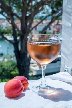 Drinking of cold rose wine from Provence with red apricots and view on yacht harbour of Port Grimaud, summer vacation on French Riviera, France
