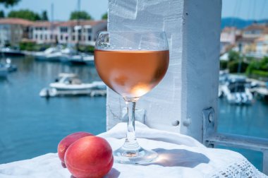 Drinking of cold rose wine from Provence with red apricots and view on yacht harbour of Port Grimaud, summer vacation on French Riviera, France