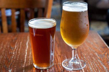 Pint glasses of cold fresh british ale and lager beer served in old vintage English pub