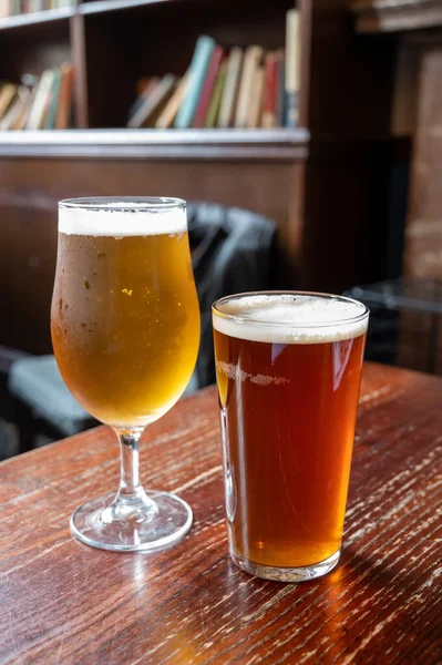 Pint glasses of cold fresh british ale and lager beer served in old vintage English pub