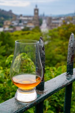 Glass of single malt scotch whisky and view from Calton hill to park and old parts of Edinburgh city in rainy summer day, Scotland, UK