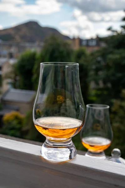 Glass of single malt scotch whisky served on old window sill in Scottisch house with view on old part of Edinburgh city, Scotland, UK, dram of blended whiskey