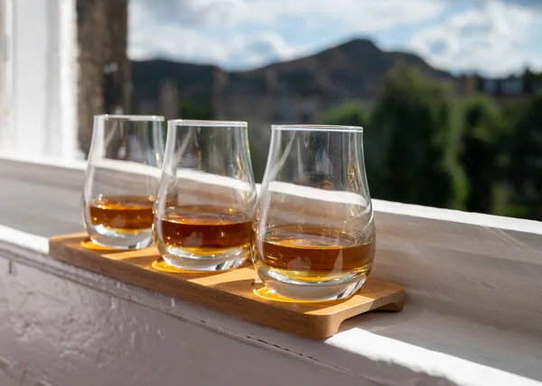 Flight of single malt scotch whisky served on old window sill in Scottisch house with view on old part of Edinburgh city, Scotland, UK, dram of whiskey