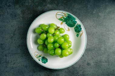 Fotokopi alanı olan gri arka planda bir kase yeşil üzüm. Üst Manzara. Karanlıkta ateş etmek. Yazmak için yer.