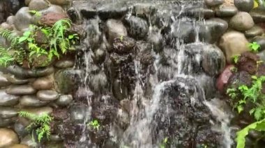 Bahçede küçük dekoratif bir şelale. Temiz su taşların üzerinden akıyor. Peyzaj tasarımı.