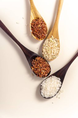 Raw and uncooked rice assortment in wooden spoon on white background. Place for text. Top view.
