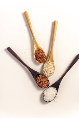 Raw and uncooked rice assortment in wooden spoon on white background. Place for text. Top view.