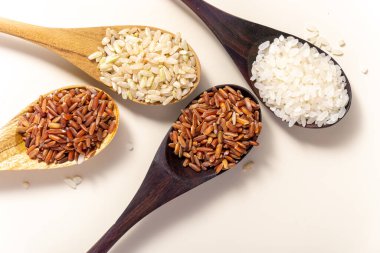 Raw and uncooked rice assortment in wooden spoon on white background. Place for text. Top view.