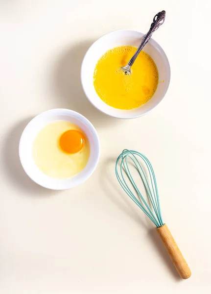 Egg beat, Egg Shell with Whisk. Raw eggs in a glass and white bowl on the table. Flat lay. Broken White Background.