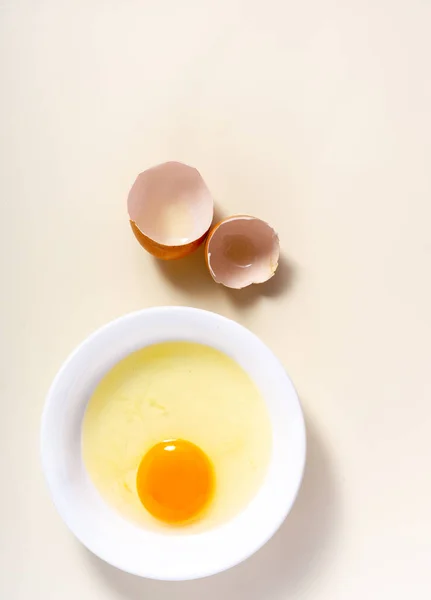 Raw eggs and egg shell in a glass bowl on the table. Top View. Broken White Background.