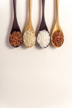 Raw and uncooked rice assortment in wooden spoon on white background. Place for text. Top view.