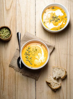 Ahşap zemin üzerinde bir dilim ekmek dilimli sarı balkabağı çorbası. Yatay olarak. Üst görünüm.