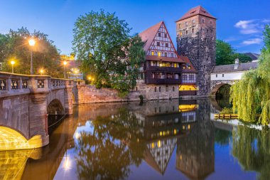 Nuremberg, Franconia, Almanya 'da Pegnitz nehrinin kıyısındaki yarı keresteli eski evlerin renkli ve pitoresk bir manzarası gece aydınlandı.