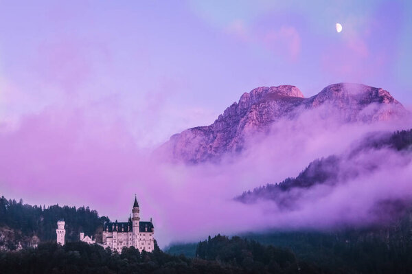 Neuschwanstein castle under the moon in the evening, with the mountain and the mist in the background
