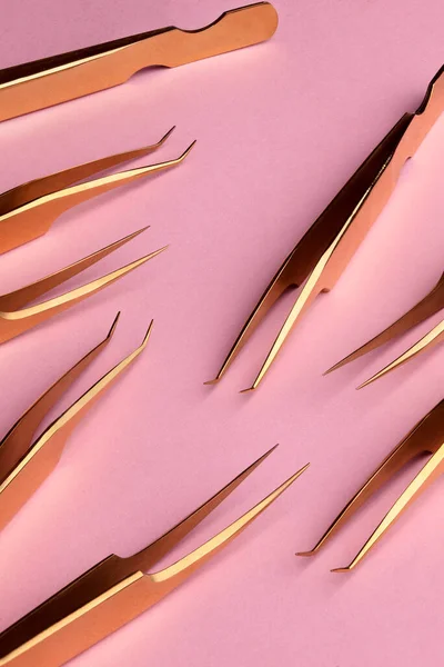 Herramientas de oro para el procedimiento de extensión de pestañas. Pinzas doradas sobre fondo rosado. Concepto de belleza y moda — Foto de Stock