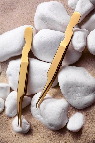 Két arany csipesz fehér köveken a homokon.Golden Tools for Eyelash Extension Procedure. .Rózsaszín háttér. Szépség és divat reklám koncepció — Stock Fotó