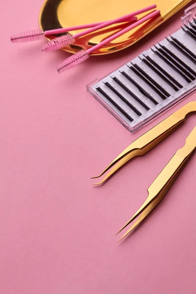 Herramientas de oro para el procedimiento de extensión de pestañas. Pinzas doradas, palete con pestañas, pinceles para pestañas en placa dorada. Fondo rosado. Concepto de belleza y moda — Foto de Stock