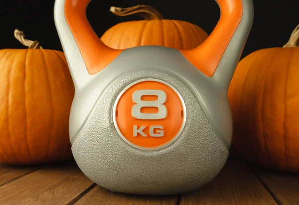 Heavy kettlebell with orange pumpkins. Healthy fitness and gym lifestyle, autumn or fall composition for Halloween and Thanksgiving.