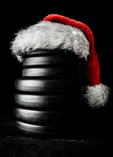 Gym dumbbell barbell weight plates stacked on top of each other in shape of a snowman, with red Santa Claus hat. Healthy fitness Christmas concept.