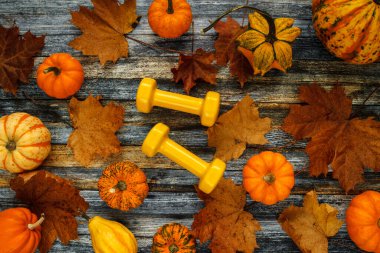 Two yellow dumbbells with various pumpkins, squashes and autumn leaves. Healthy fitness lifestyle flat lay composition. Fall gym concept for Halloween or Thanksgiving.