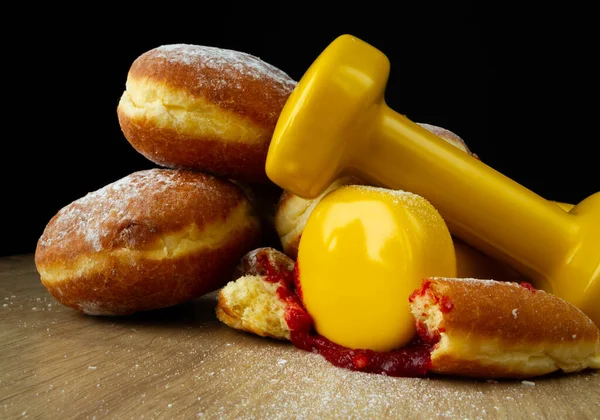 Gym dumbbells crushing Polish paczki deep-fried doughnuts. Fat Thursday (Tlusty czwartek). Paczek, traditional feast day in Poland. Healthy fitness gym workout, cheat day temptation vs sticking to diet.