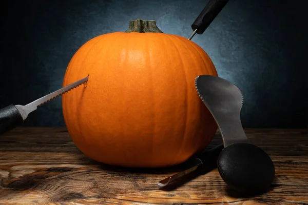 Halloween pumpkin carving tools for Jack-o\'-lantern face cut out. Spoon gutter and saw blades, with whole orange autumn pumpkin.