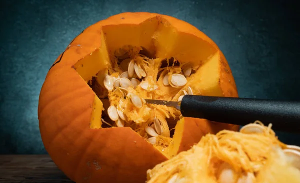 Halloween pumpkin gutting before carving Jack-o\'-lantern. Guts and seeds inside a pumpkin being removed with saw knife blade carve tool, through cut off top lid.