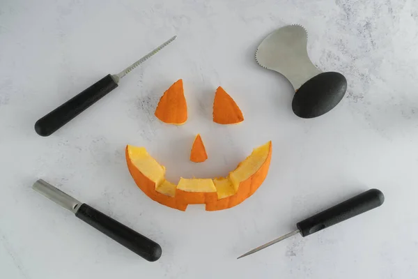 Halloween pumpkin pieces. Spooky laughing, scary carved Jack Lantern eyes, nose, mouth. Jack-o'-lantern elements with carving tools - spoon, saw blade, pointed and grove carver.