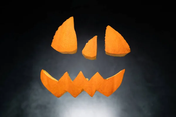 Halloween pumpkin face cut out pieces floating in the air. Flying carved eyes, nose and mouth elements.
