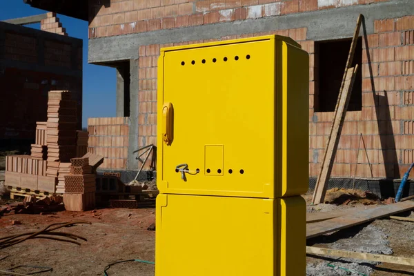 Yellow metal gas connection box at the construction site of a new single-family house. Unfinished stand-alone home building under construction.