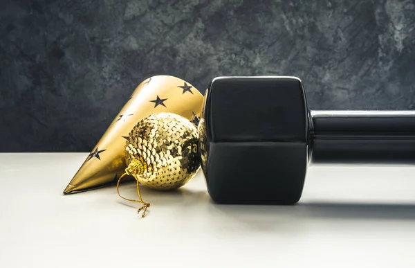 Heavy black dumbbell, golden decoration and a party hat for New Year\'s Eve celebration. Healthy fitness lifestyle concept. Gym and workout New Year\'s resolution.