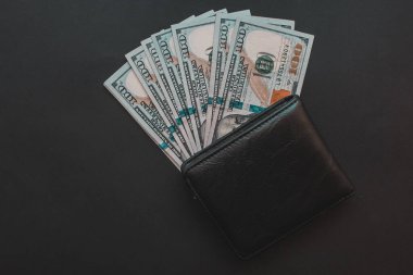 Siyah arka planda cüzdanı olan dolarlar..