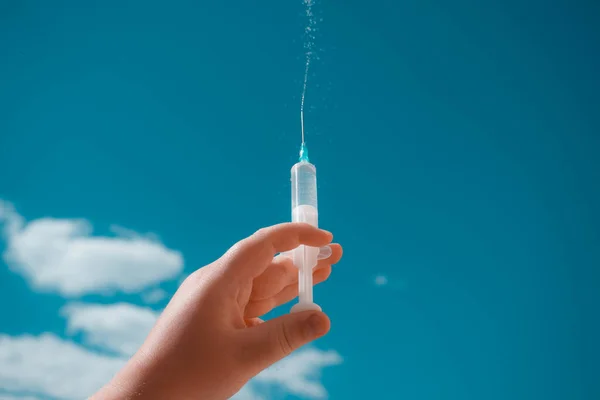 Doctor holding syringes in hands on sky background.